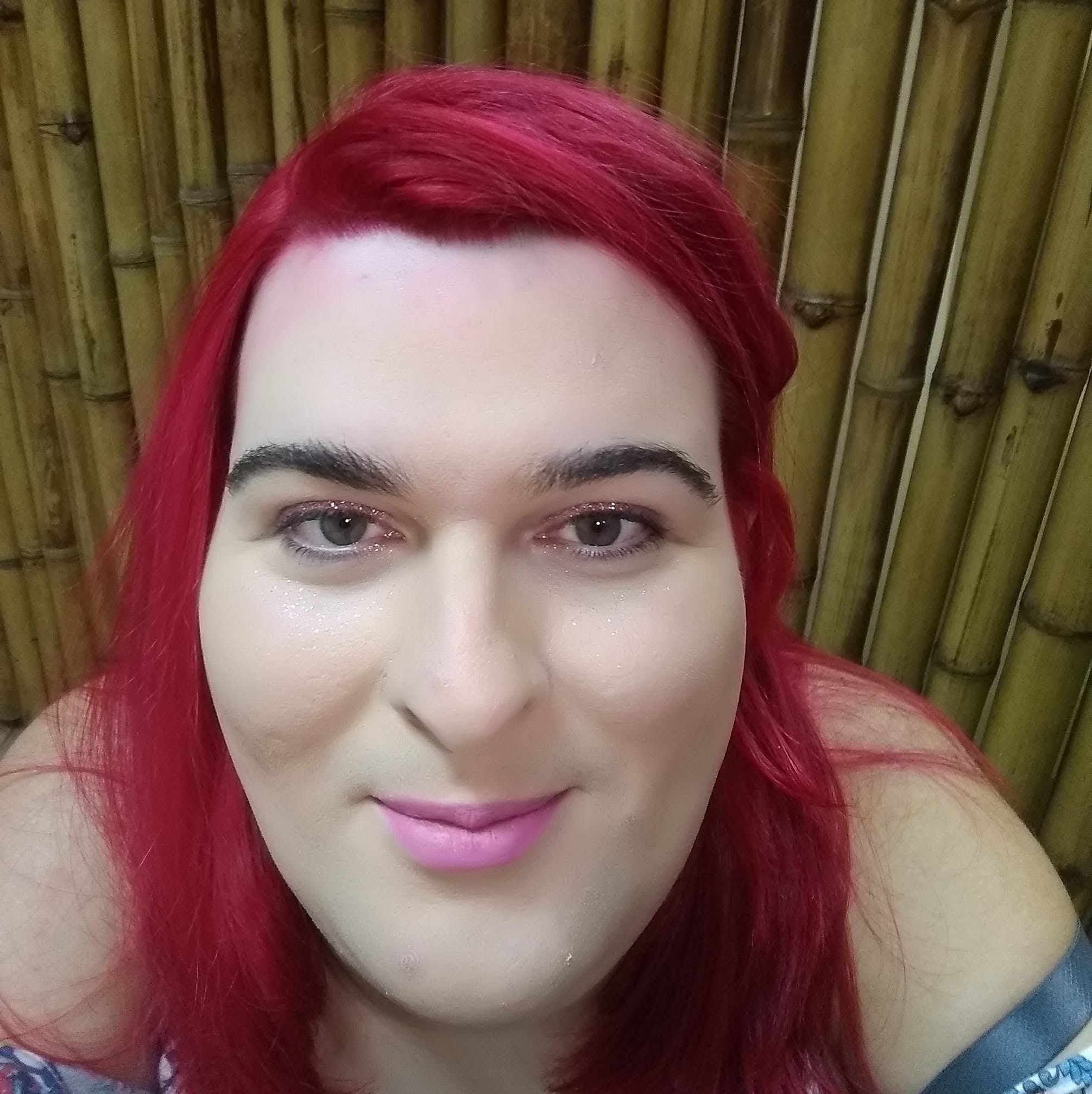 Retrato de Paloma sorrindo com cabelo vermelho vibrante diante de um painel de bambu